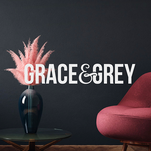 Grace & Grey logo overlaid on an interior design photo with a pink feather vase arrangement and a mauve armchair against a dark grey wall.