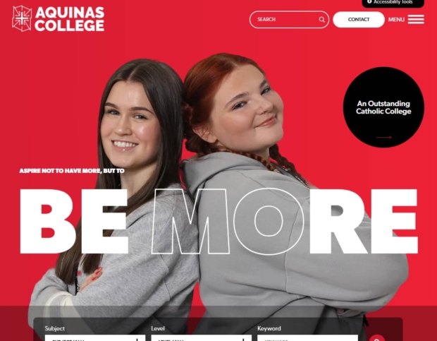 Aquinas College website homepage banner featuring two smiling students in grey hoodies against a red background, with the tagline 'Aspire not to have more, but to be more.